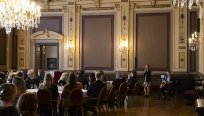 Ihmiset istuvat Raatihuoneen salissa puheen aikana.