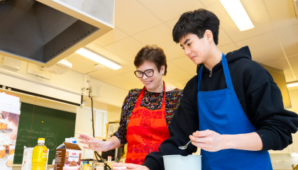 Kaksi henkilöä on leivontatarvikkeiden ääressä esiliinat edessään.