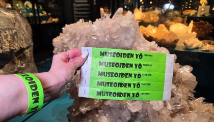 Vihreitä Museoiden yö -rannekkeita kuvan etualalla ja henkikön ranteessa. Taustalla kiviä näyttelytilassa.