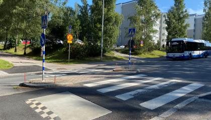 Suojatie ja hidasteet kuvattu kesällä ja bussi näkyy taustalla lähestyvän suojatietä.