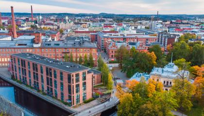Ilmakuva Tampereen keskustasta, jossa näkyvät Tammerkosken punatiiliset tehdasrakennukset, syksyinen puistoalue ja kaupungin siluetti.