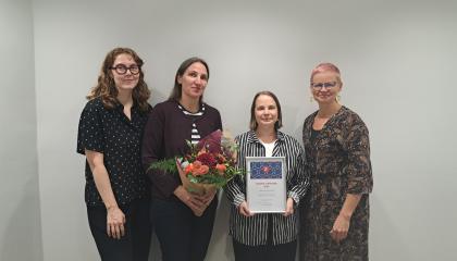 Lastenkirjainstituutin neljän työntekijää. Yhdellä on kädessään kukkakimppu, toisella diplomi. 