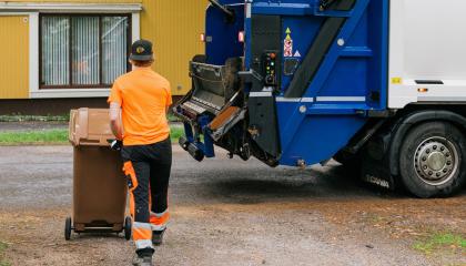 Kuvassa tyhjennysauto ja kuljettaja siirtämässä jäteastiaa. 