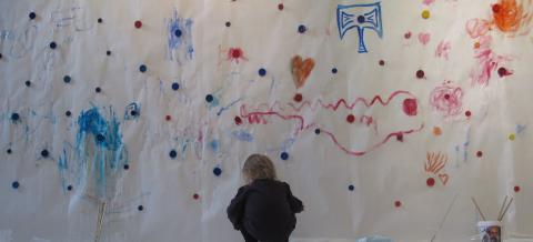 Pieni tyttö maalaa seinään vesivärillä.