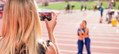 Nainen ottaa valokuvaa kahdesta urheilijasta yleisurheilukisoissa Ratinassa.