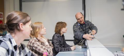 Three persons follow when one shows them the function of on technical item on board.