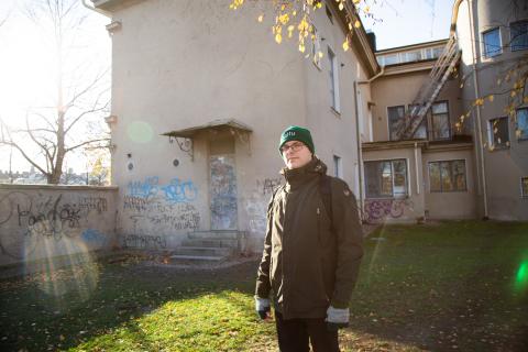 Mies katsoo kameraan ja taustalla vaalea rakennus.