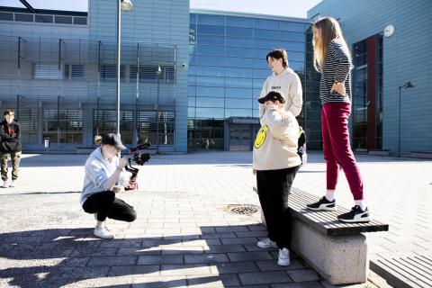 Opiskelija ottaa valokuvaa kolmesta opiskelijasta pihalla.