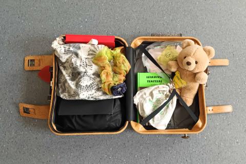 Avonainen matkalaukku, jonka sisällä nalle-pehmolelu ja draamapaketin pussukoita joiden sisällä paketin tavaroita.