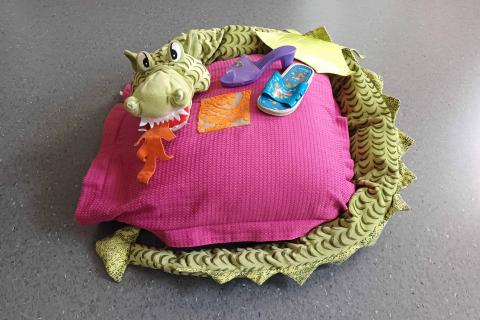Vaaleanpunainen tyyny, jonka päällä pehmo-lohikäärme ja parittomat lasten kengät.