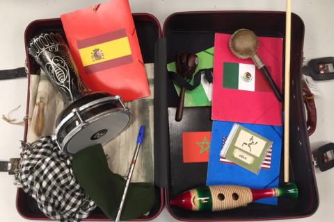 Aukinainen matkalaukku, jonka sisällä rumpu, helisitin, huivi, kansioita ja guiro.