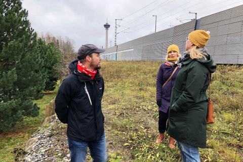 Kolme henkilöä seisoo syksyisellä niityllä.