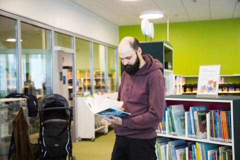 Joni Trivedi seisoo ja lukee kirjaa kirjaston lastenosastolla.