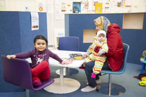 Äiti ja kaksi pientä tytärtä istuvat kirjastossa lasten leikkipaikalla.