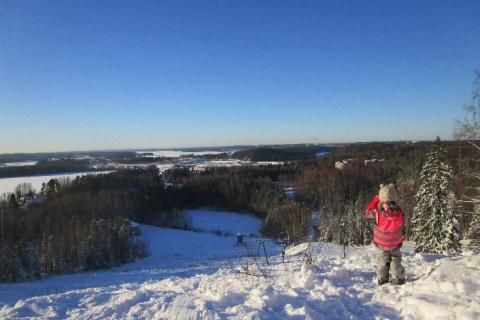 A child is standing on a high snow-covered hill, looking out over the landscape.