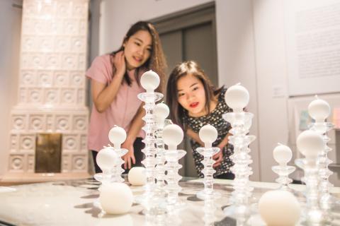 Kaksi naista tarkastelee lasisia kynttilänjalkoja museon näyttelyssä.
