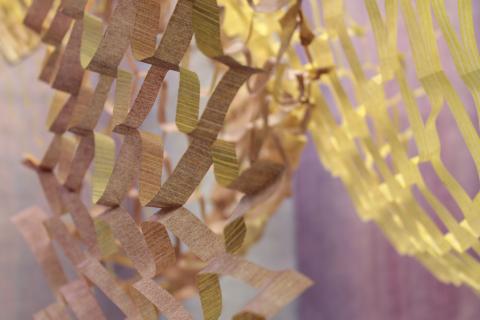 Keltaisesta paperista on leikattu verkkomaista kuviota. Sen takana hohtaa violetti valo.