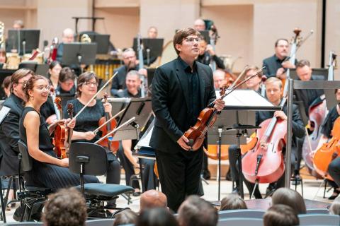 The Tampere Philharmonic Orchestra&#039;s musicians sitting with their instruments in the concert hall, Johannes Põlda standing with his violin and facing the audience.