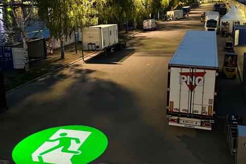 Trucks and trailers on the banks of the Ratina estuary at night. The emergency exit sign is projected onto the surface of the street.