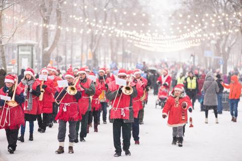 Trumpeters and other people marching down the street in red costumes and hats.