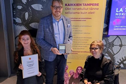 Tampereen Ratikan toimitusjohtaja vastaanottamassa esteettömyyspalkintoa kahdelta esteettömyystyöryhmän jäseneltä. Heistä toinen on lyhytkasvuinen ja toinen istuu pyörätuolissa.
