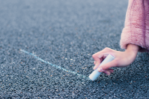 Nuori käsi piirtää vaaleansinistä viivaa liidulla asfaltille.