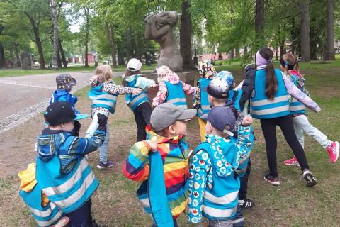 Joukko lapsia on patsasmaisissa asennoissa Aleksanterin kirkkopuiston Suru-veistoksen vieressä.