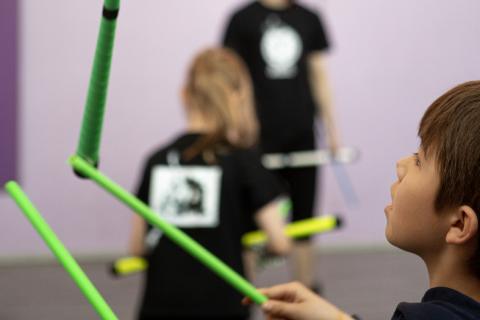 Koululainen harjoittelee Devi Stick -sirkusvälineen käyttöä ja heittää kahden kepin avulla kolmatta ilmaan.