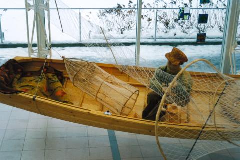Puuvene näyttelytilassa. Veneen ympärillä on koristeena verkkoja.