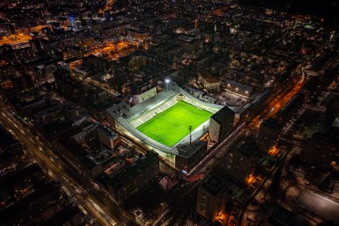 Valaistu vihreänä hohtava jalkapallokenttä Tammelan stadionilla pimeän aikaan. Kuvattu ylhäältä dronella.