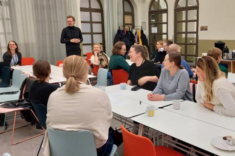 Reilu 10 projektikahveille osallistunutta ihmistä istuu kahvipöytien äärellä.