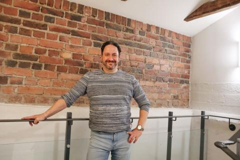 Mies seisoo tiiliseinän edessä ja hymyilee. 