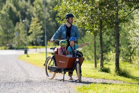 Henkilö kuljettaa laatikkopyörää, kyydissä kaksi lasta.