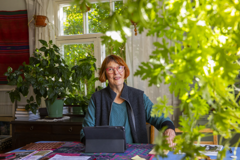 A person is sitting at a table surrounded by large green plants.