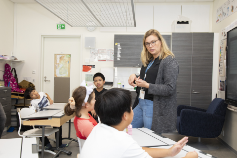 The teacher stands and talks to the students, four of whom are shown in the picture.