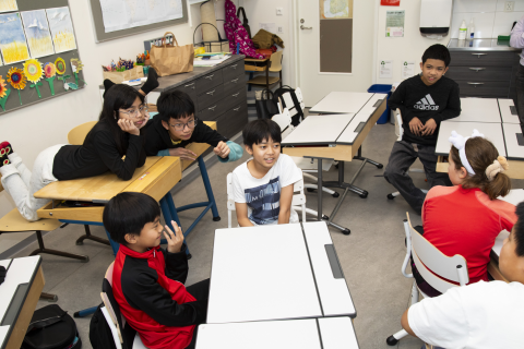Several students sit casually behind their desks and chat with each other.