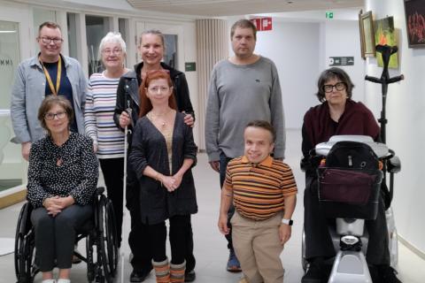 Seitsemän esteettömyystyöryhmän jäsentä yhdessä ryhmän sihteerin kanssa ryhmäkuvassa. Kaksi jäsenistä istuu pyörätuolissa. Kaksi muuta on lyhytkasvuisia.