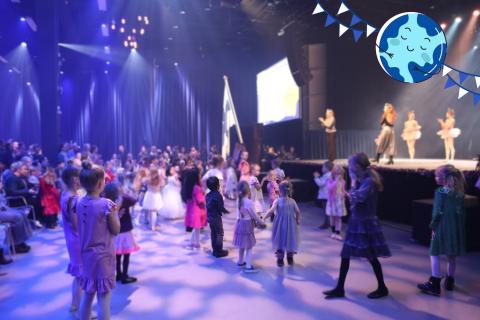 Lapsia tanssimassa lavan edessä. Lavalla tanssinohjaajia opastamassa tanssimaan. 