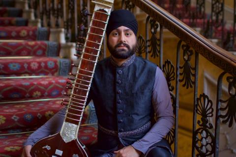 Intialaisvaikutteisessa kuvassa mies istuu rappusilla sitar-soitin vierellään.