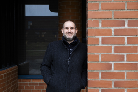 A person is leaning against a red brick wall.