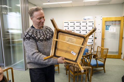 Henkilö nostaa vanhaa tuolia ja näyttää sen pohjaa.