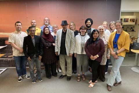 Photo of the members of the Tampere City Immigrant Council for 2026 in a group photo indoors. The individuals are posing in two rows in front of a neutral, warm-toned background.