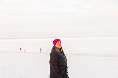 Henkilö seisoo lumisella jäällä. Takana menee retkiluistelijoita.