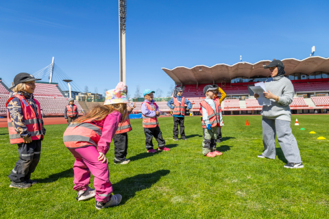 Seitsemän lasta leikkii Sumaya Haidarianin ohjeiden mukaisesti Ratinan stadionin nurmikentällä.