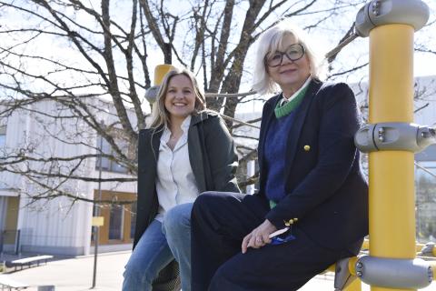 Two cheerful women sitting on the edge of a fence.