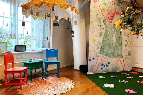 A small red and blue chair and a small green table in the middle. A yellow parasol above the chairs and table.