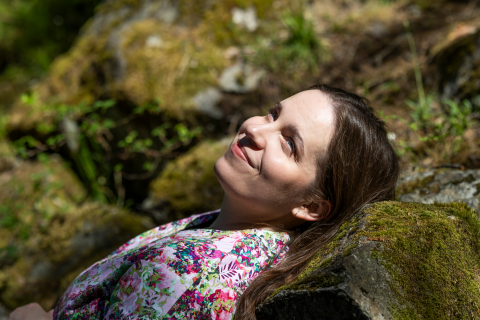 A person rests their head against a moss-covered rock and looks up, smiling.