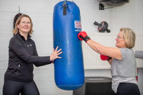 A woman is punching a punching bag that another woman is holding.