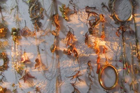 A work of art featuring dried flowers, gold-colored jewellery, small frames, and an angel pendant.