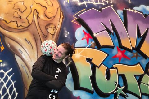 A man with a ball on his shoulder in front of the World Cup football exhibition.
